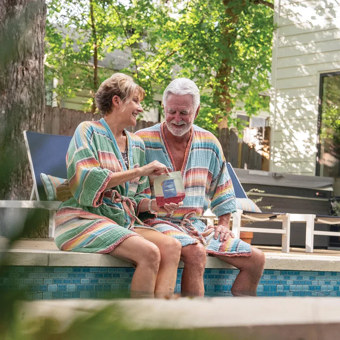Couple poolside in robes holding a pouch of Hometown Hero Balance Strawberry 1:1 THC:CBD gummies in a backyard