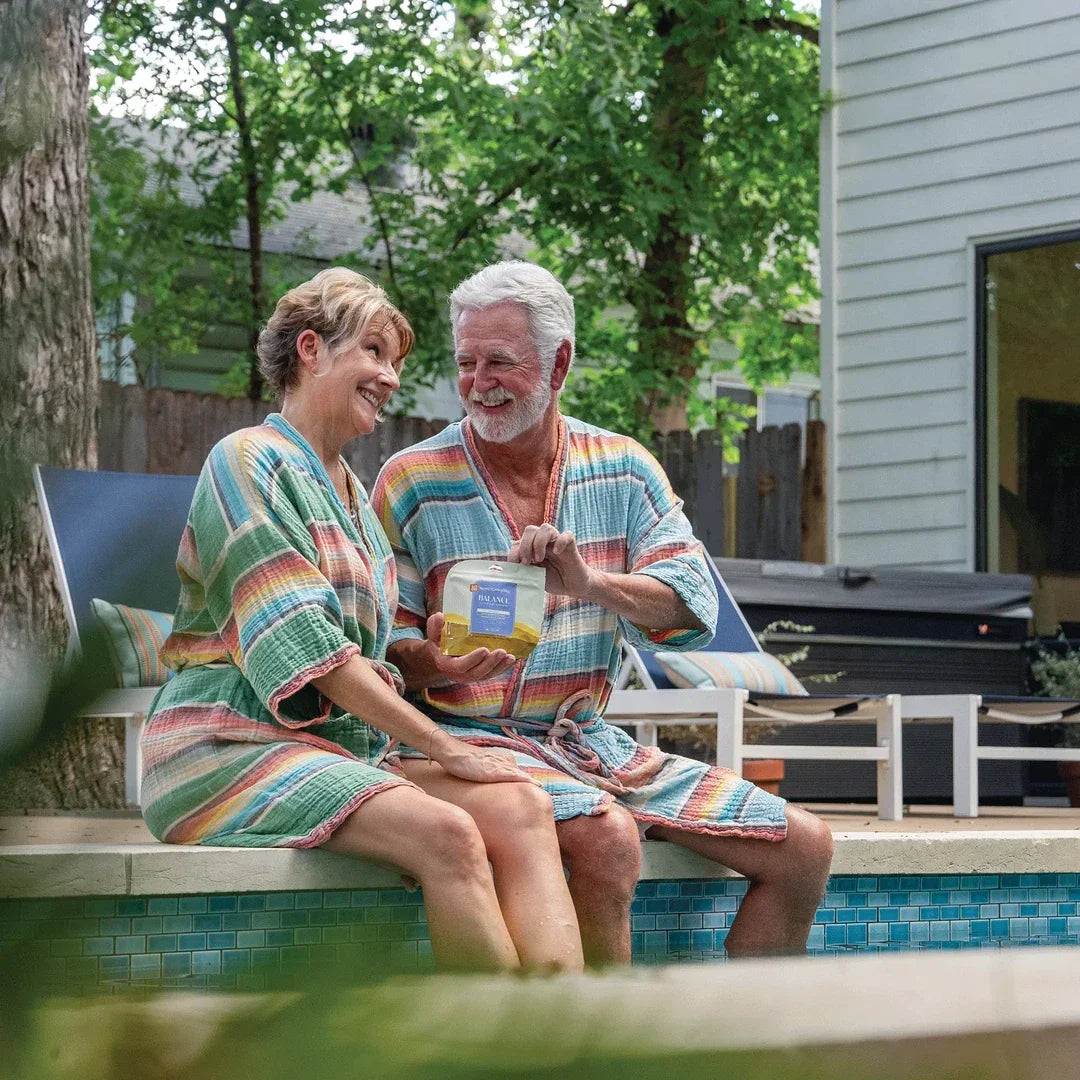 Couple in robes by a pool holding a pouch of Hometown Hero Balance Pineapple 1:1 THC:CBD gummies, lifestyle shot