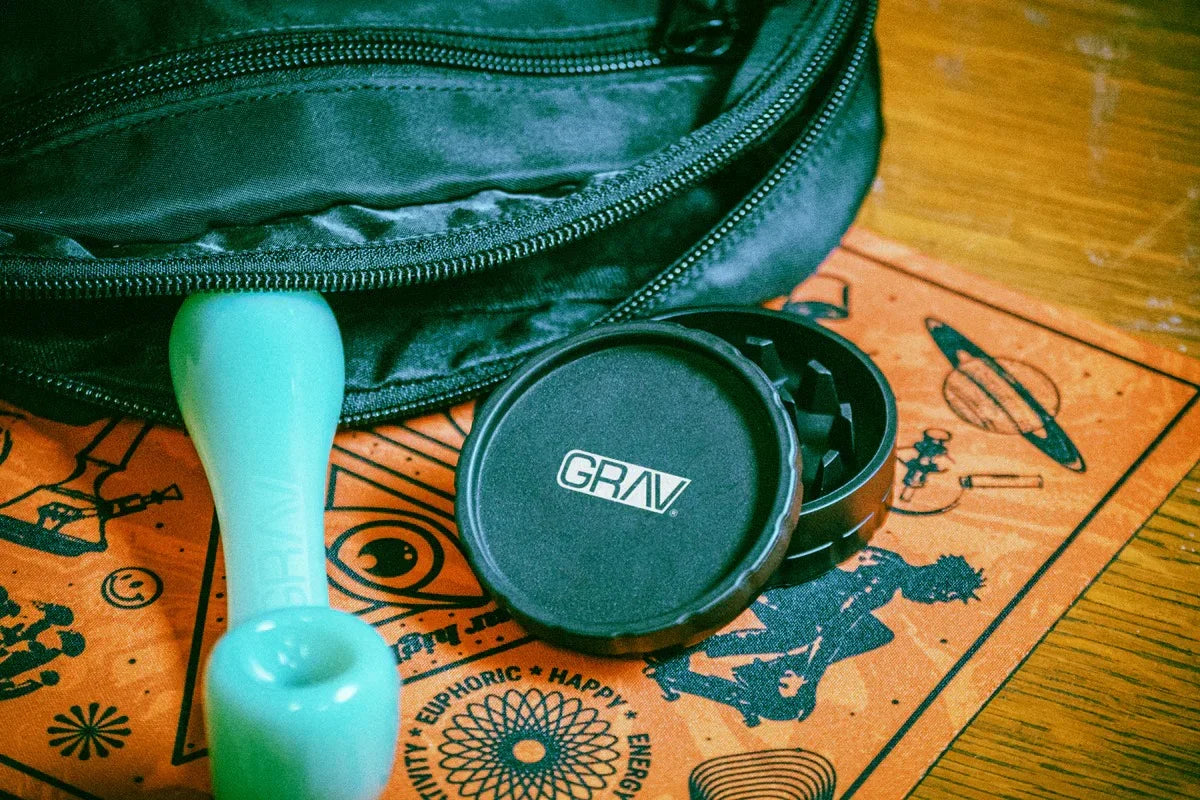 GRAV hemp plastic 2-piece grinder beside a green glass hand pipe on a printed mat and dab kit