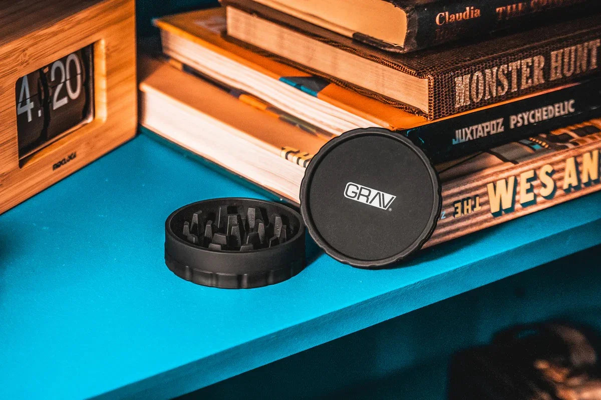 GRAV 2-piece hemp plastic grinder open on a teal shelf by stacked books and a 4:20 flip clock