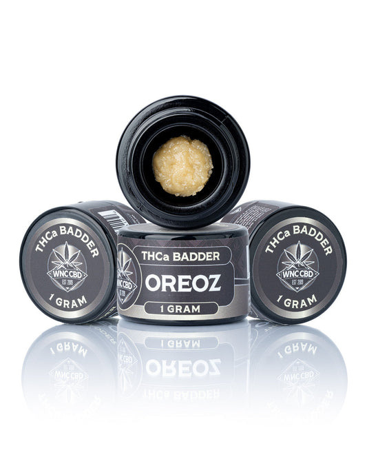 Three black 1g jars of WNC CBD Oreoz THCa badder concentrate with one open showing golden product