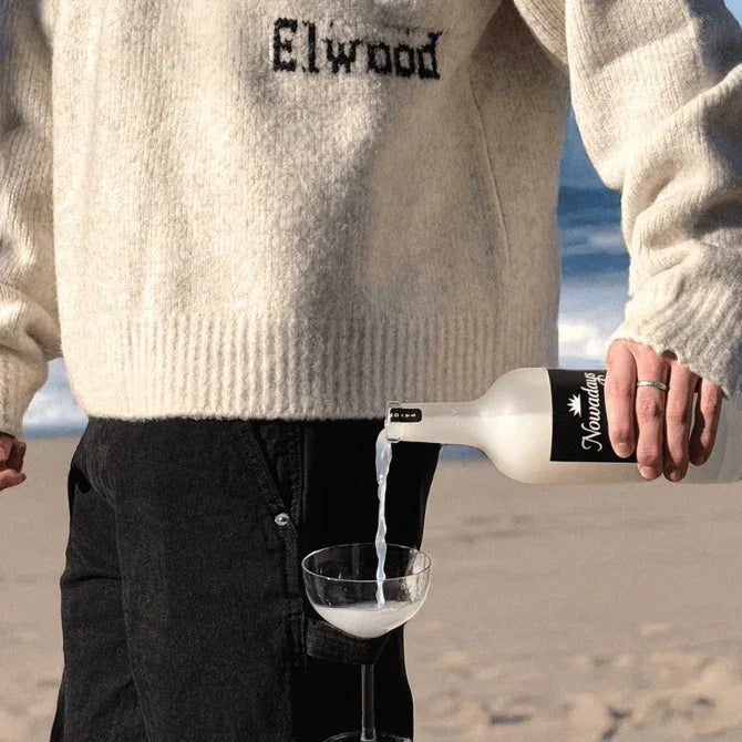 Person pouring Nowadays High Dose THC infused beverage from the frosted bottle into a coupe glass on the beach